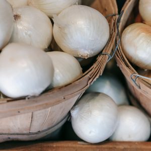 High angle of pile of fresh organic white onions in wooden baskets placed on stall in local grocery market